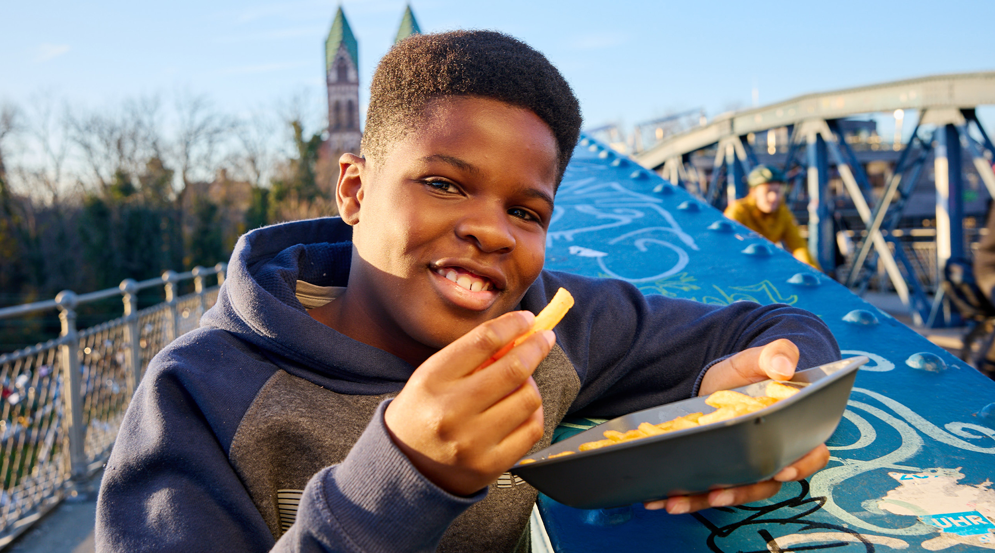 Junge isst Pommes aus einer Mehrwegschale auf einer Brücke in Freiburg