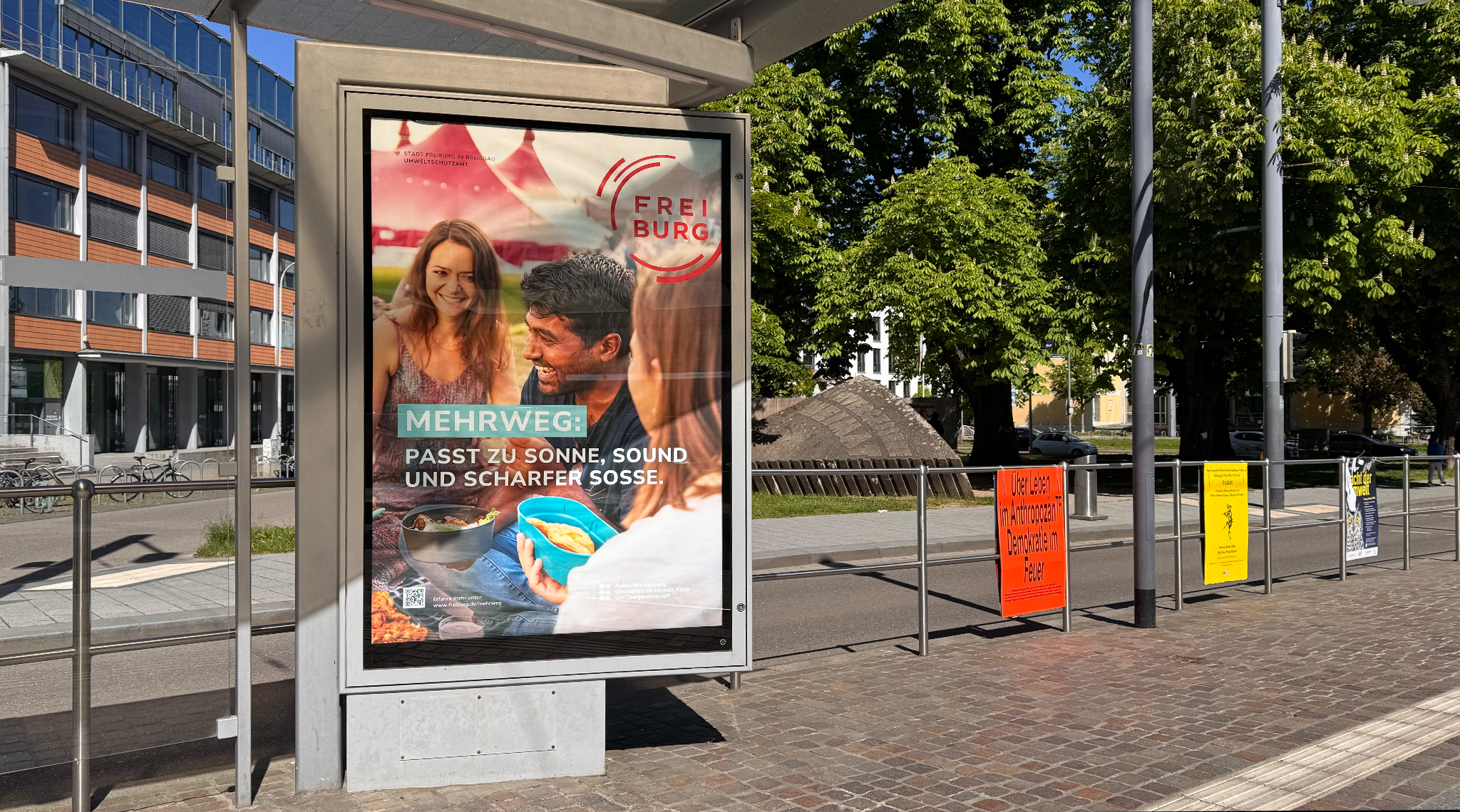 Mehrweg-Plakat an einer Haltestelle: „Passt zu Sonne, Sound und scharfer Soße.“